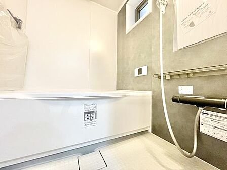 ホワイトを基調とした明るいバスルームです。壁の落ち着いた色合いが空間に調和しています。浴槽はゆったりとしたサイズ感で床のデザインにもこだわりが感じられます。浴室内には窓があり換気にも配慮されています。