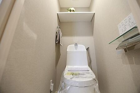 トイレはシンプルなデザインながら、使いやすい温水洗浄便座が設置されております。また、上部には便利な棚が備わっております。