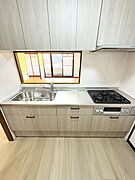 木目調の収納が上品な印象を与えシンプルでまとまりのあるデザインのキッチンです。三口コンロと広々としたシンクが備わっており使い勝手にも配慮されています。カウンター越しにリビングが見渡せる設計です。