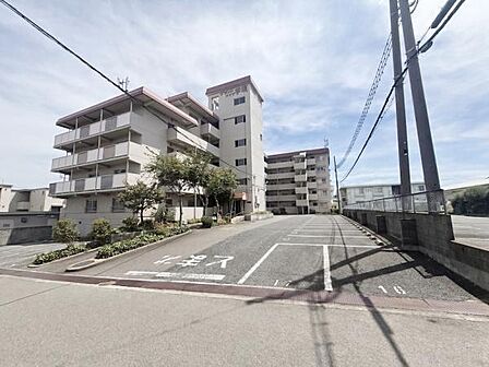 【一部AIモノ消し済み・実際の室内状況優先】シンプル建物全体が見渡せる外観写真です。敷地内には舗装された駐車スペースが確保されています。周囲の道幅もゆとりがあり出入りしやすい環境です。