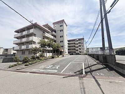 外観：【一部AIモノ消し済み・実際の室内状況優先】シンプル建物全体が見渡せる外観写真です。敷地内には舗装された駐車スペースが確保されています。周囲の道幅もゆとりがあり出入りしやすい環境です。