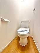 明るい色調の床材が特徴のトイレです。シンプルですっきりとしたデザインなのでお手入れもしやすくなっています。壁面にはペーパーホルダーとタオル掛けも設置されています。清潔感のある空間です。