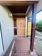 玄関は屋根付きのアプローチが特徴で雨の日でも利用しやすい設計です。落ち着いた色合いのタイル床が清潔感を演出しています。重厚感のある木製ドアと外壁の組み合わせが外観に調和をもたらしています。