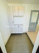 玄関にはシンプルなデザインの収納が設置されており使い勝手の良い空間です。清潔感のあるタイル床が特徴です。ドアと収納の色合いが統一され落ち着いた印象を与えます。