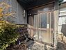 玄関：玄関部分には落ち着いた色合いのタイルとすりガラスが使用されています。屋根付きで雨の日も安心です。周囲には植物もあり自然を感じられる空間となっています。
