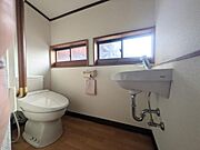 窓から自然光と自然な風が入るトイレです。手洗い器が壁付けでスペースが有効活用されています。二つの小窓が換気にも配慮されています。床の木目調が落ち着いた雰囲気を演出します。