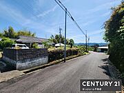 前面道路は広々としており車の通行もスムーズです。周囲には自然が多く開放感があります。道路沿いの景観もすっきりと整っています。現地の雰囲気が分かる一枚です。