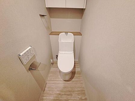 温水洗浄便座と吊戸棚を備えた清潔感あるトイレ空間。収納も確保され、日用品の整理もしやすい設計です。