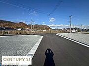 広々とした前面道路が特徴の現地写真です。周辺には自然を感じられる山々が広がっています。道路の舗装も新しく清潔感があります。整備された区画が印象的です。開放感にあふれるロケーションです。