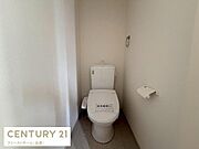 窓から光が入る明るいトイレです。白を基調としたシンプルなデザインで清潔感があります。ペーパーホルダーやタオルリングが設置されています。温水洗浄便座を備えています。