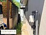 その他：住居の側面には給湯器が設置されており外構のスペースも確保されています。日当たりがあり通気性も良い印象です。建物の外壁や配管も明るい印象を与えています。周囲の目隠しとなる壁も設けられています。