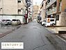 その他：周辺には飲食店や店舗が点在する前面道路の写真です。舗装された道路が続き車両の通行もスムーズです。両側に建物が立ち並び都市的な雰囲気を感じられます。整然とした町並みが広がっています。