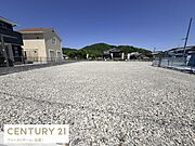 広々とした敷地が特長の現地土地写真です。周囲には住宅が建ち並び開放感があります。整地済みのため活用しやすい状態です。空と緑のコントラストが印象的です。