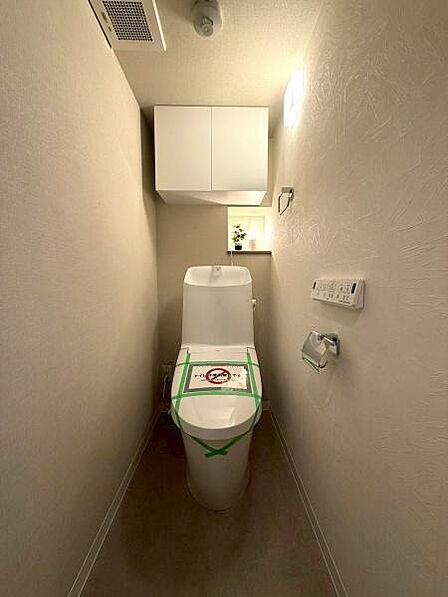 【トイレ】温水洗浄便座付きのトイレです。上部の吊戸棚に加え、奥には小物を飾れるニッチ棚があり、実用性とデザイン性を兼ね備えています。