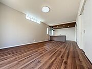 リビングは木目調のフローリングが印象的で広々とした空間が広がっています。天井の照明や高窓からの光もポイントです。キッチンと一体感のあるレイアウトが魅力的です。