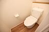 トイレ：清潔感のある内装のトイレです。手入れがしやすいシンプルなデザインとなっています。ナチュラルな床材が落ち着いた雰囲気を演出しています。壁には収納スペースも備わっています。