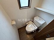 窓付きで換気しやすいトイレです。収納棚があり備品の整理にも便利です。温水洗浄便座が設置されています。シンプルな内装で清潔感があります。