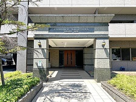 御影石調の重厚なエントランスポーチに刻まれた「FLORENCE NAGATSUKA GRAND ARK」の文字と趣あるランプが灯るエントランスが高級ホテルのような雰囲気を漂わせています。