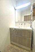 清潔感のある洗面台が特徴的です。大きな鏡が空間を広く見せてくれます。収納スペースも充実しており整理しやすい設計です。明るい照明で日常の使い勝手も良好です。木目調のデザインが落ち着いた印象を与えます。